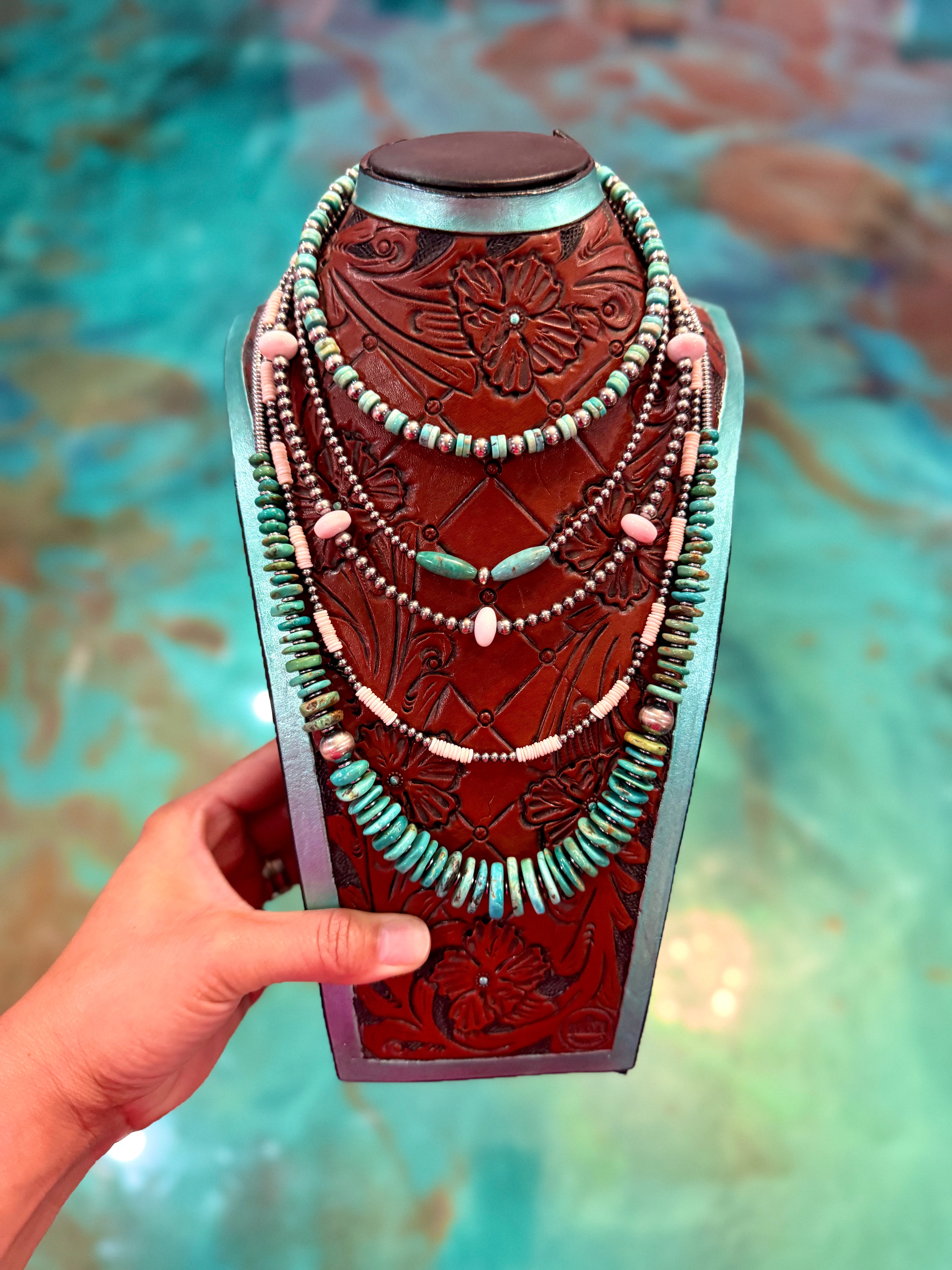 Hand holding a decorative leather and bead necklace against a blurred background