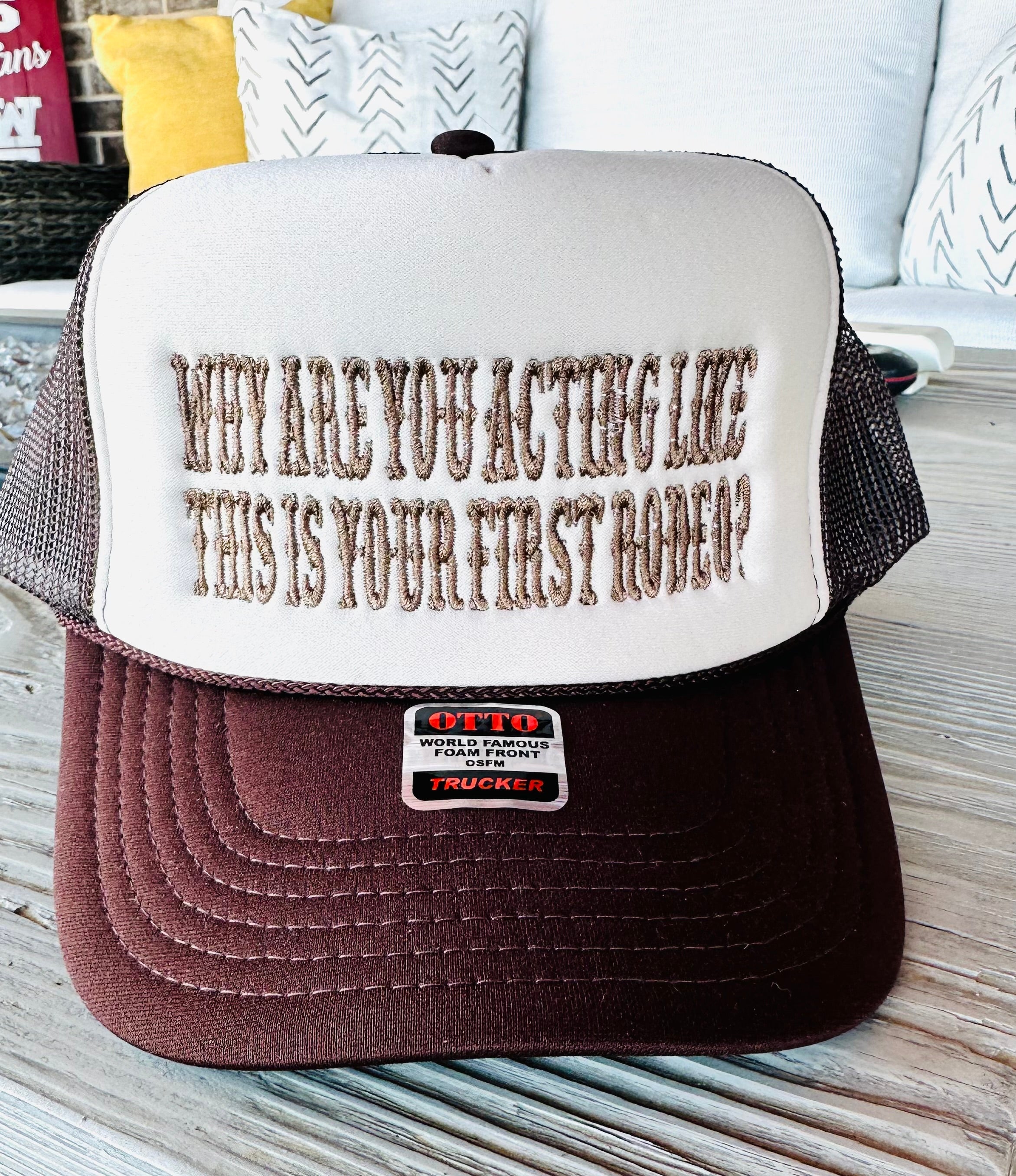 Trucker hat with text 'Why are you acting like this is your first rodeo?' on a wooden surface.