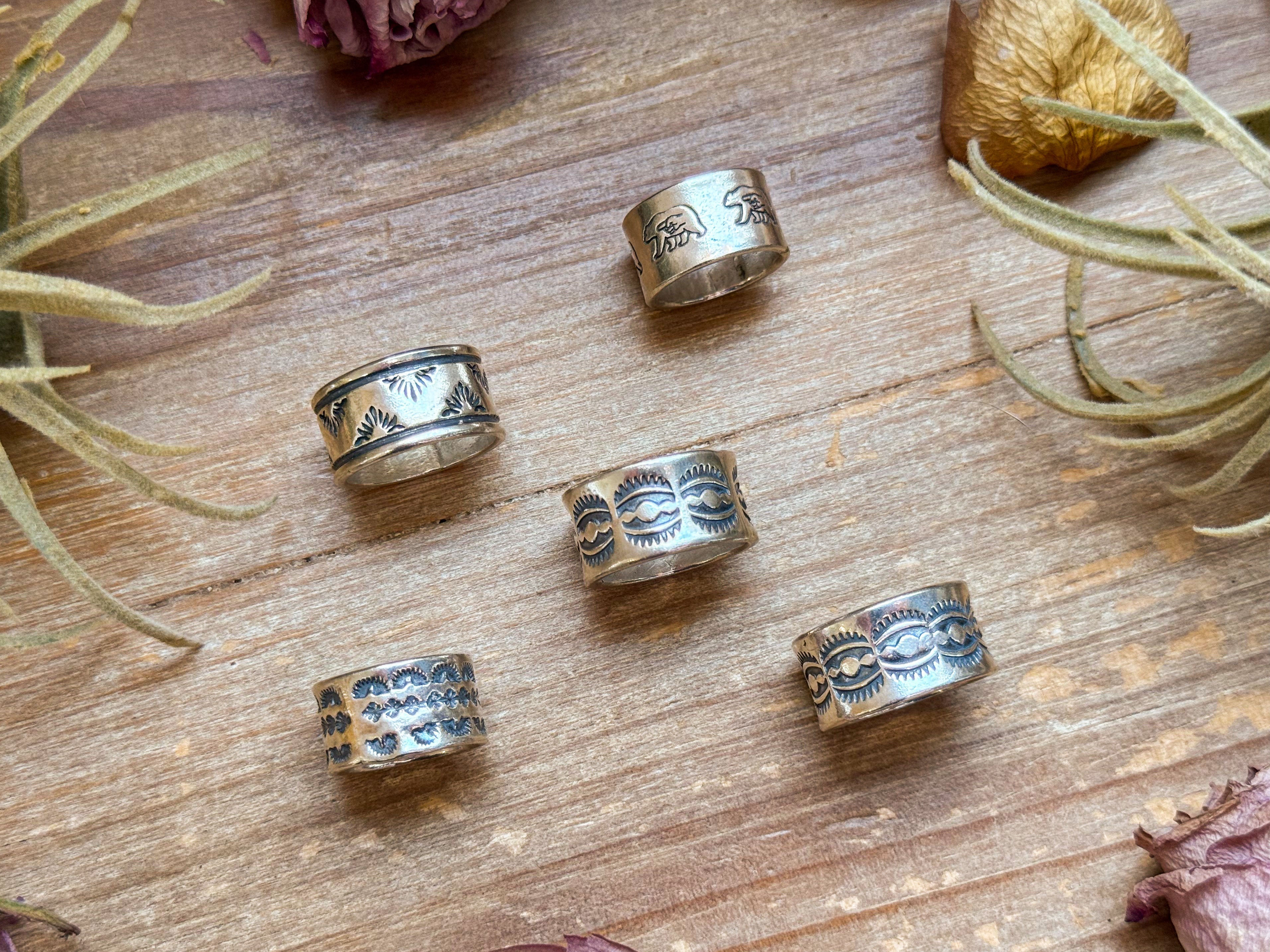 Silver rings with engraved designs on a wooden surface with plants.