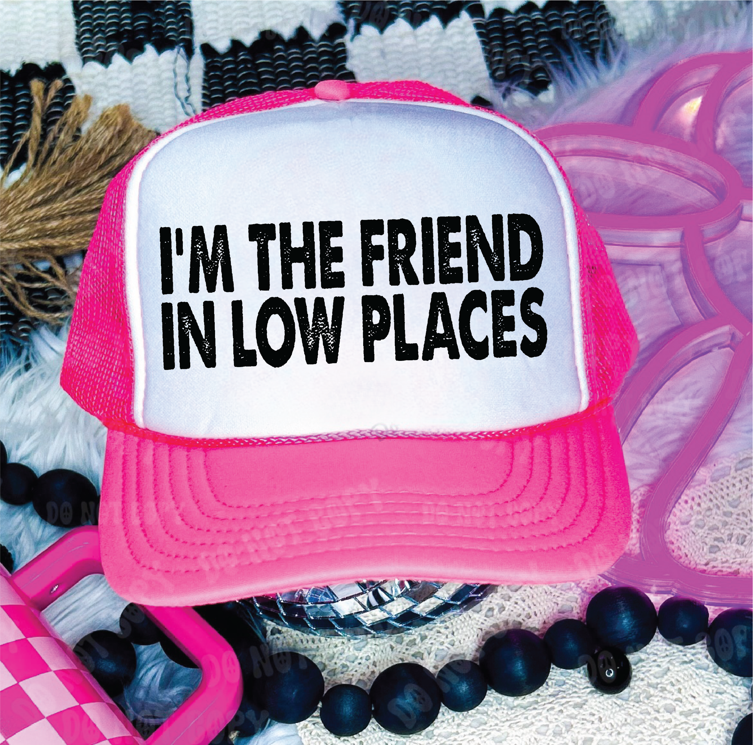 Pink and white trucker hat with text 'I'm the friend in low places' on a textured surface.