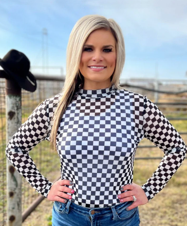Woman wearing a black and white checkered long-sleeve top with a blurred outdoor background