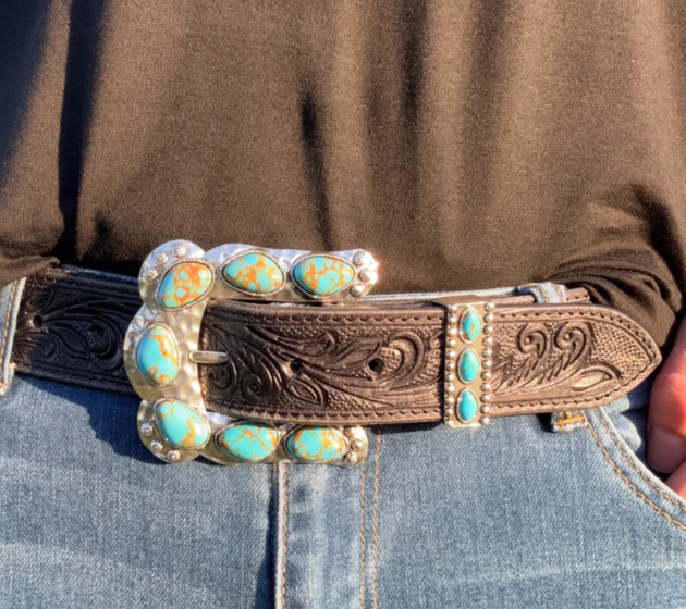 A belt featuring a detailed brown leather strap with a silver buckle adorned with turquoise stones, worn over blue jeans.