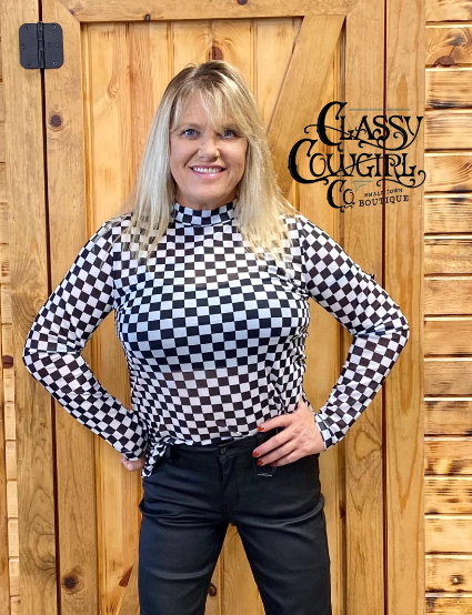 Woman wearing a black and white checkered shirt standing in front of a wooden background with 'Classy Cowgirl Co. Boutique' branding.