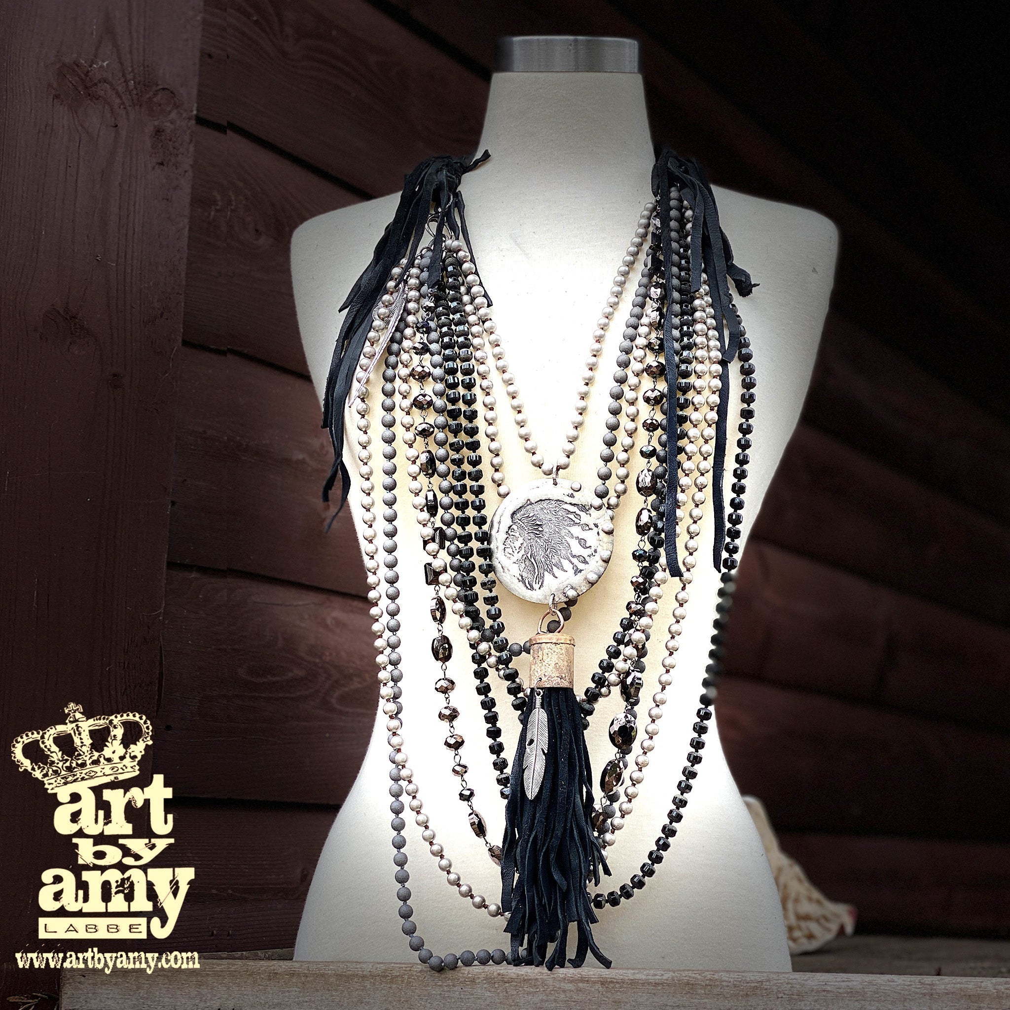 A mannequin showcasing a necklace with a leather strap and a large, hand-made chief pendant, accompanied by multiple strands of beads and a leather tassel.
