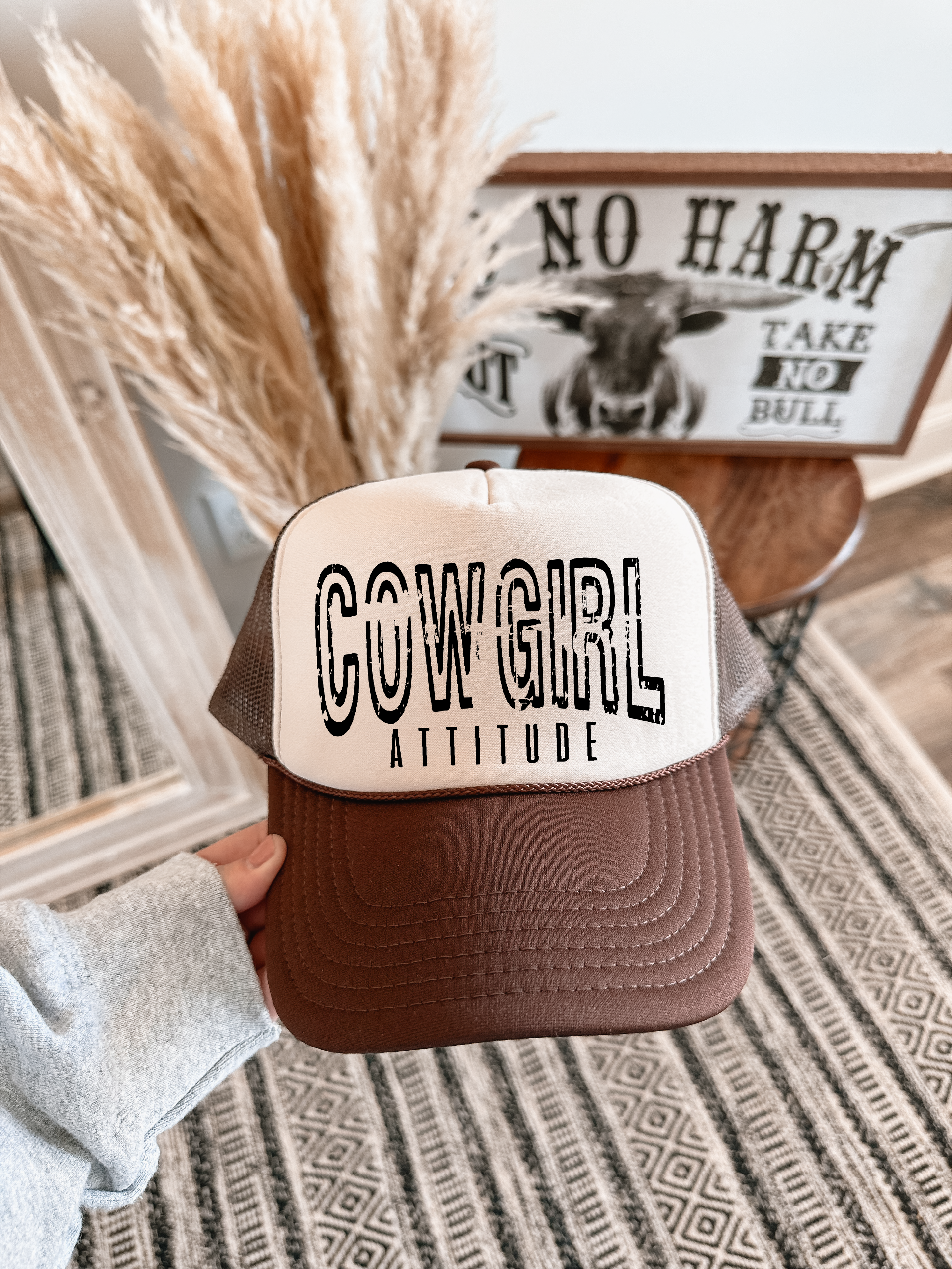 Trucker hat with 'Cowgirl Attitude' text held in front of decorative elements.
