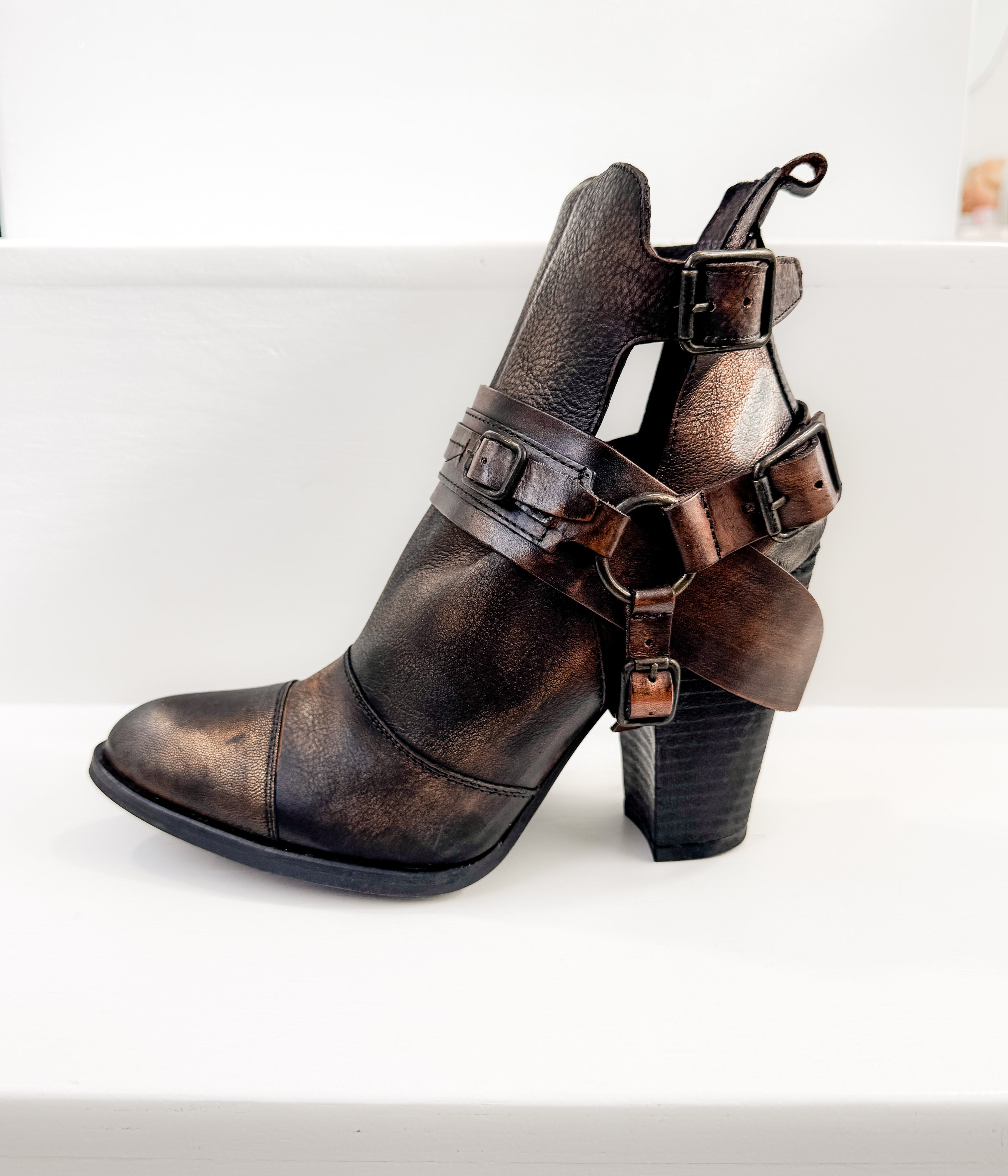 Brown leather boot with strap details on a white background