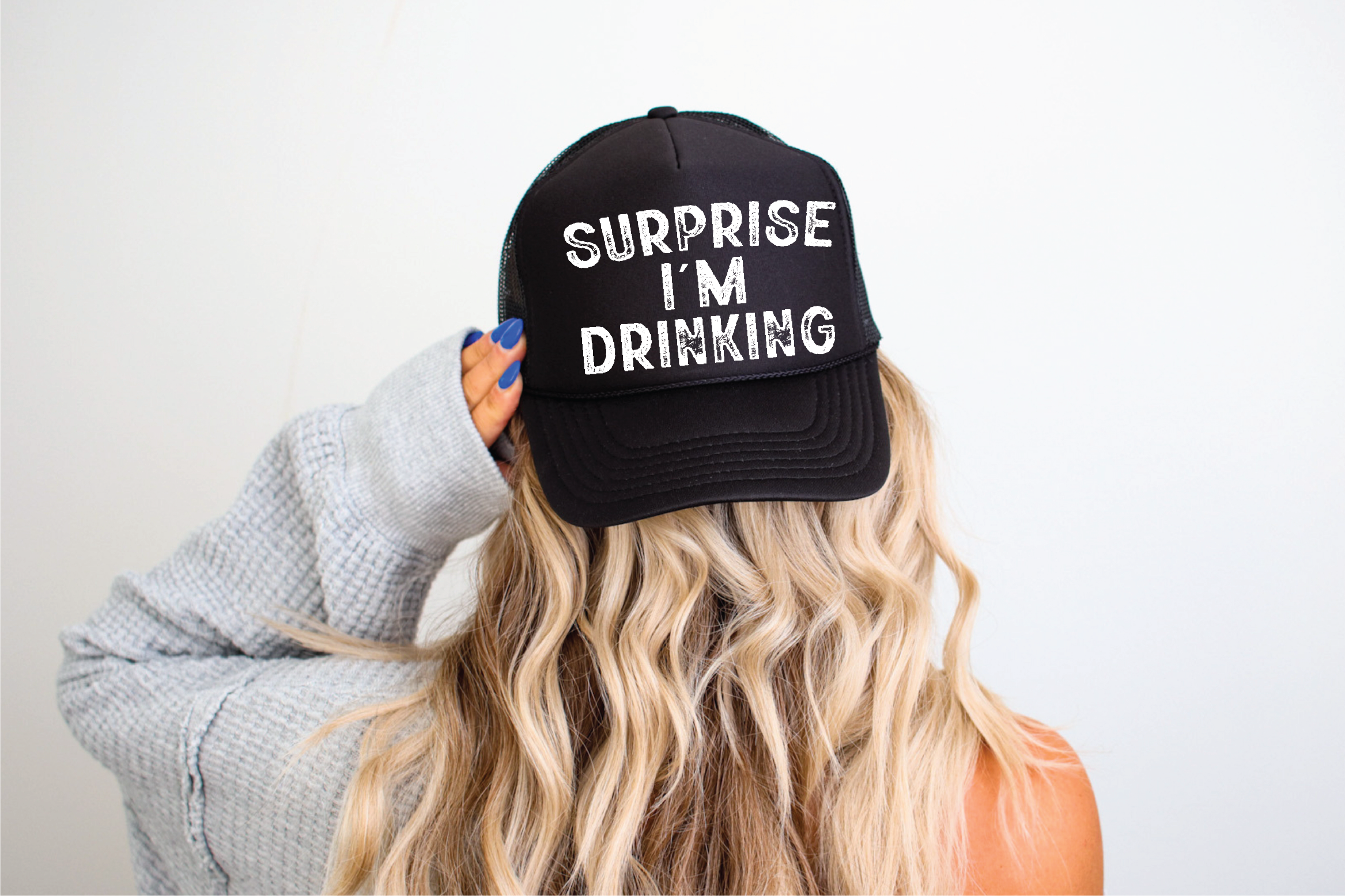Person wearing a black cap with 'Surprise I'm Drinking' text on a plain background