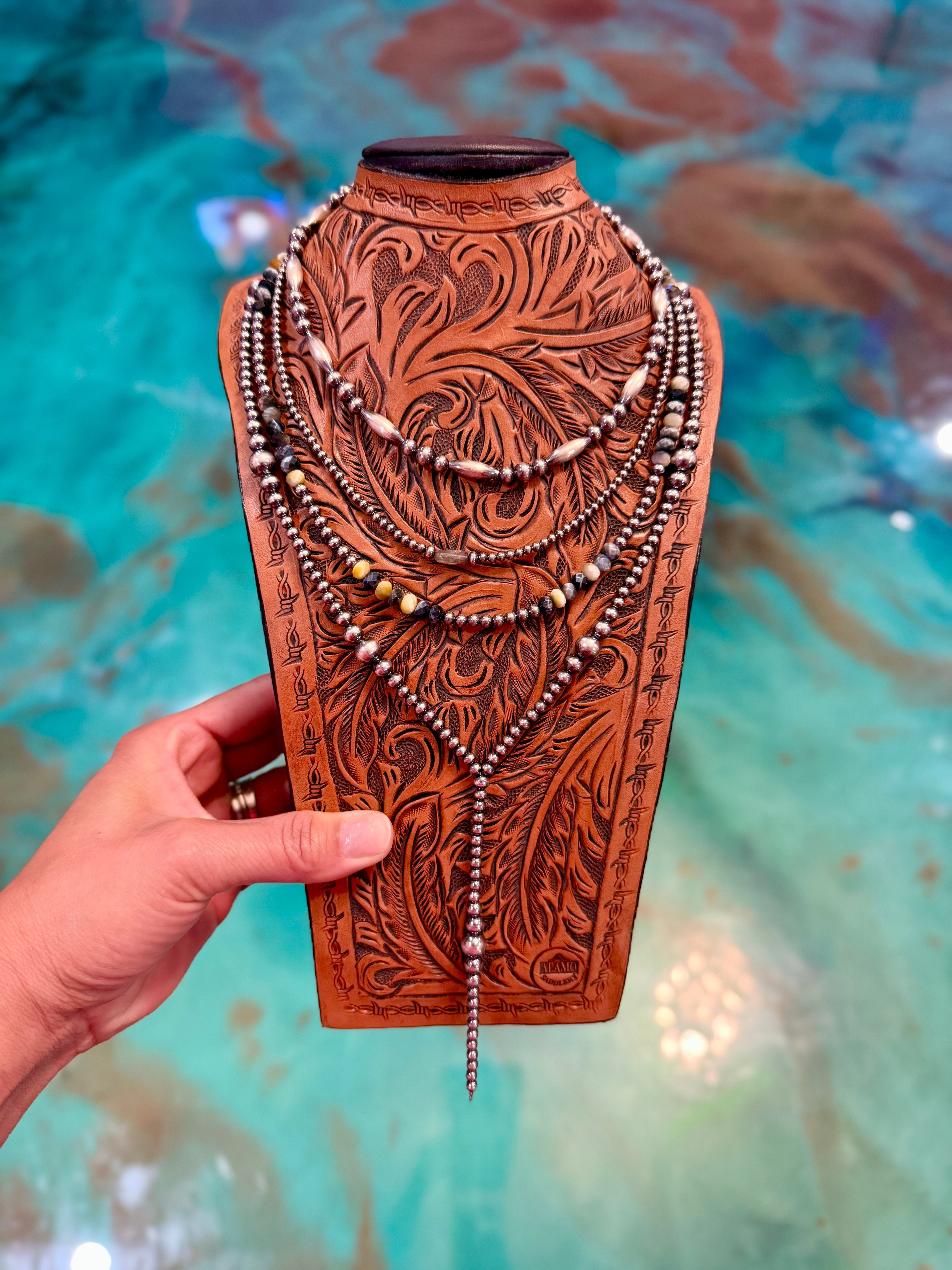 Hand holding a necklace on a decorative wooden stand with a colorful background