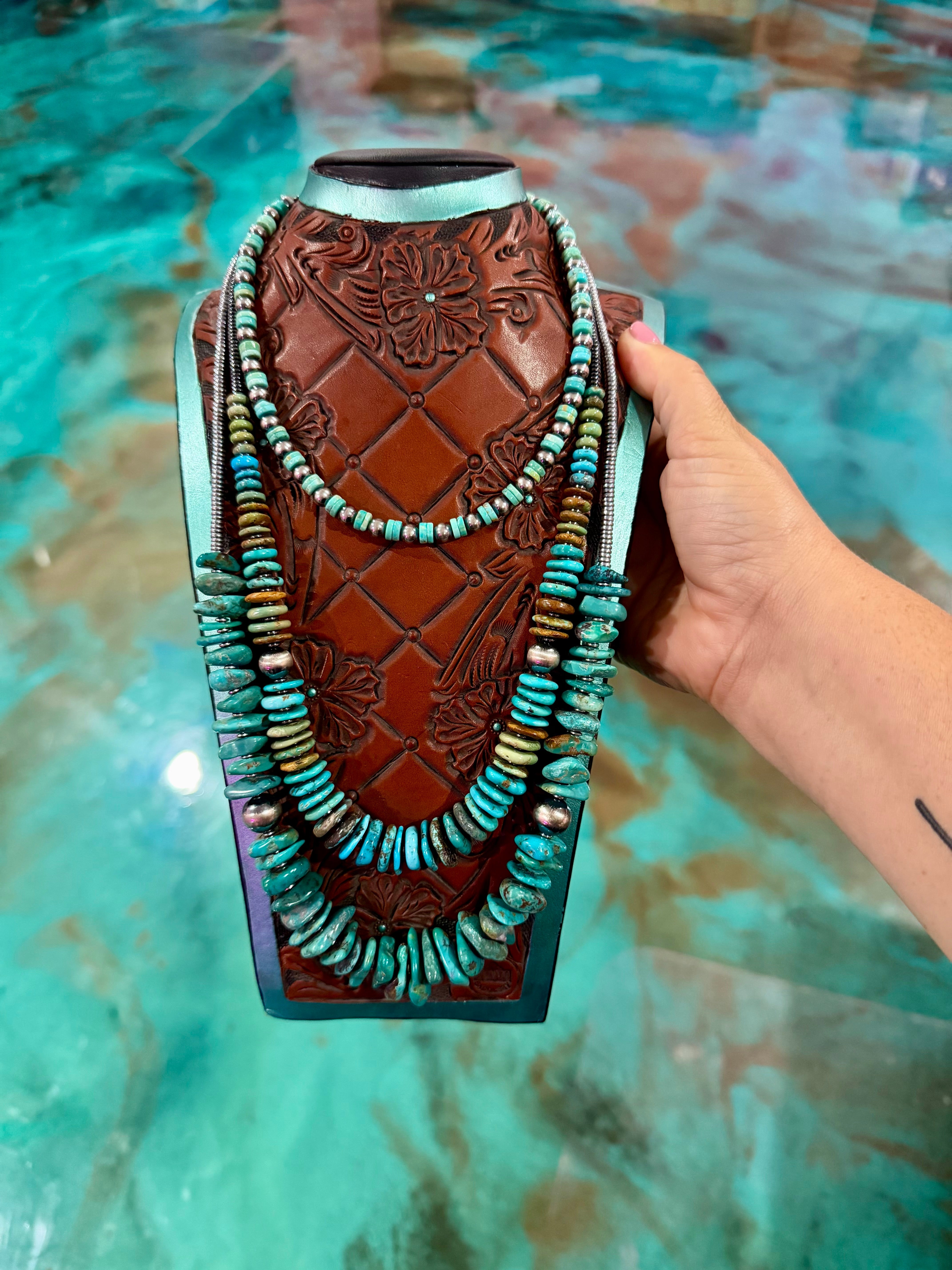 Hand holding a decorative item with intricate carvings and turquoise beads against a textured teal background