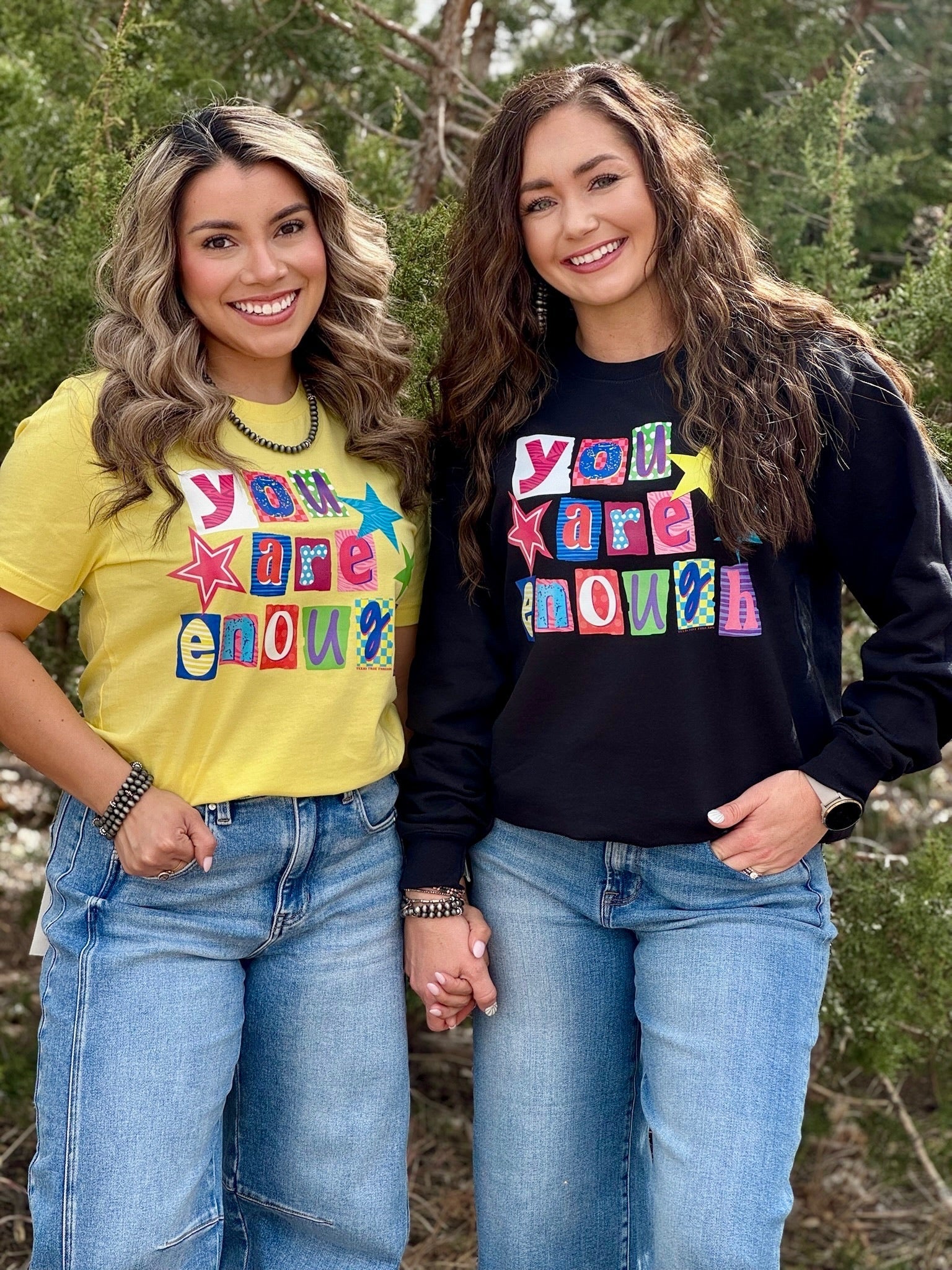 Two women wearing matching shirts with colorful text outdoors.