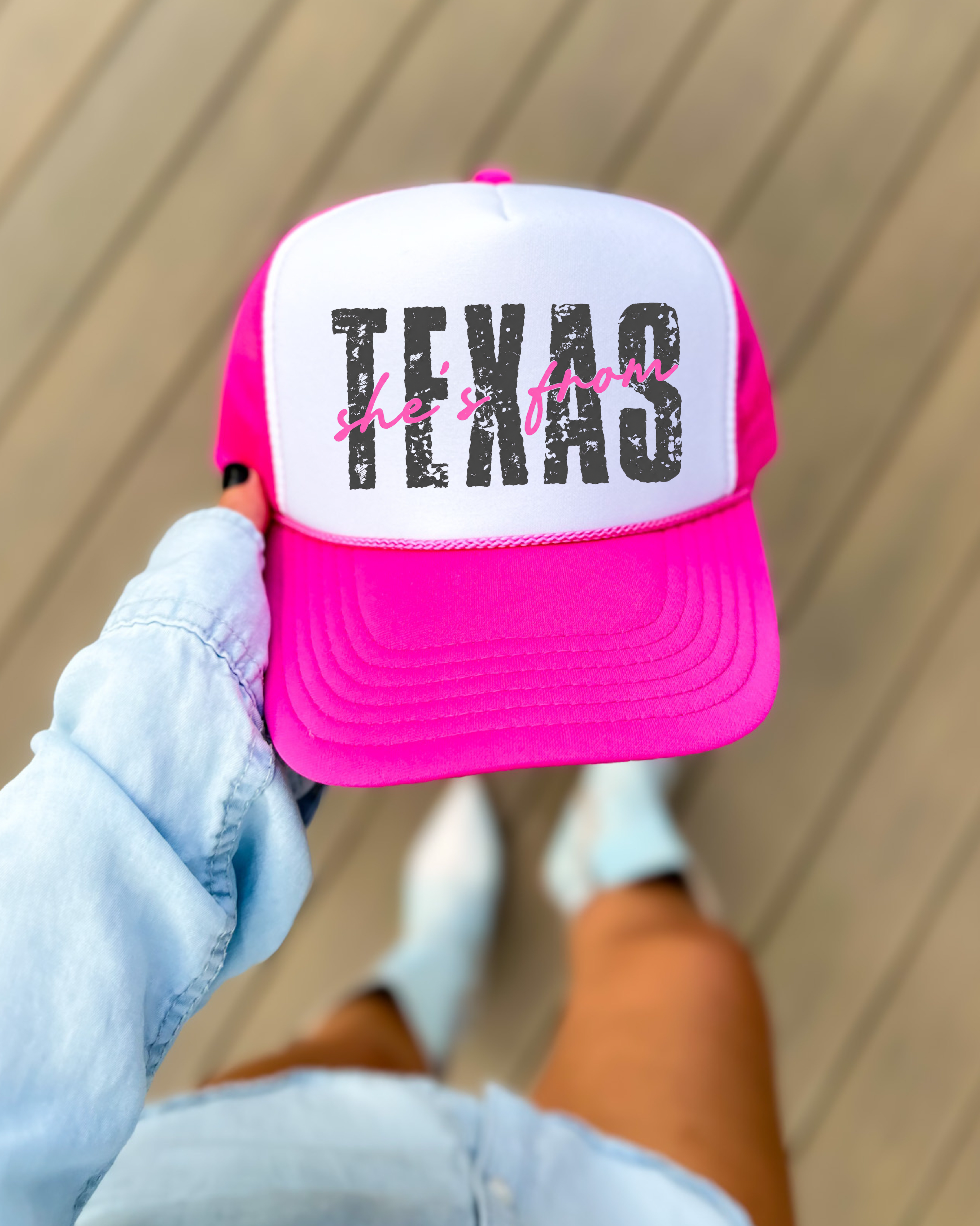 Pink and white cap with 'TEXAS she's from' text held by a person.
