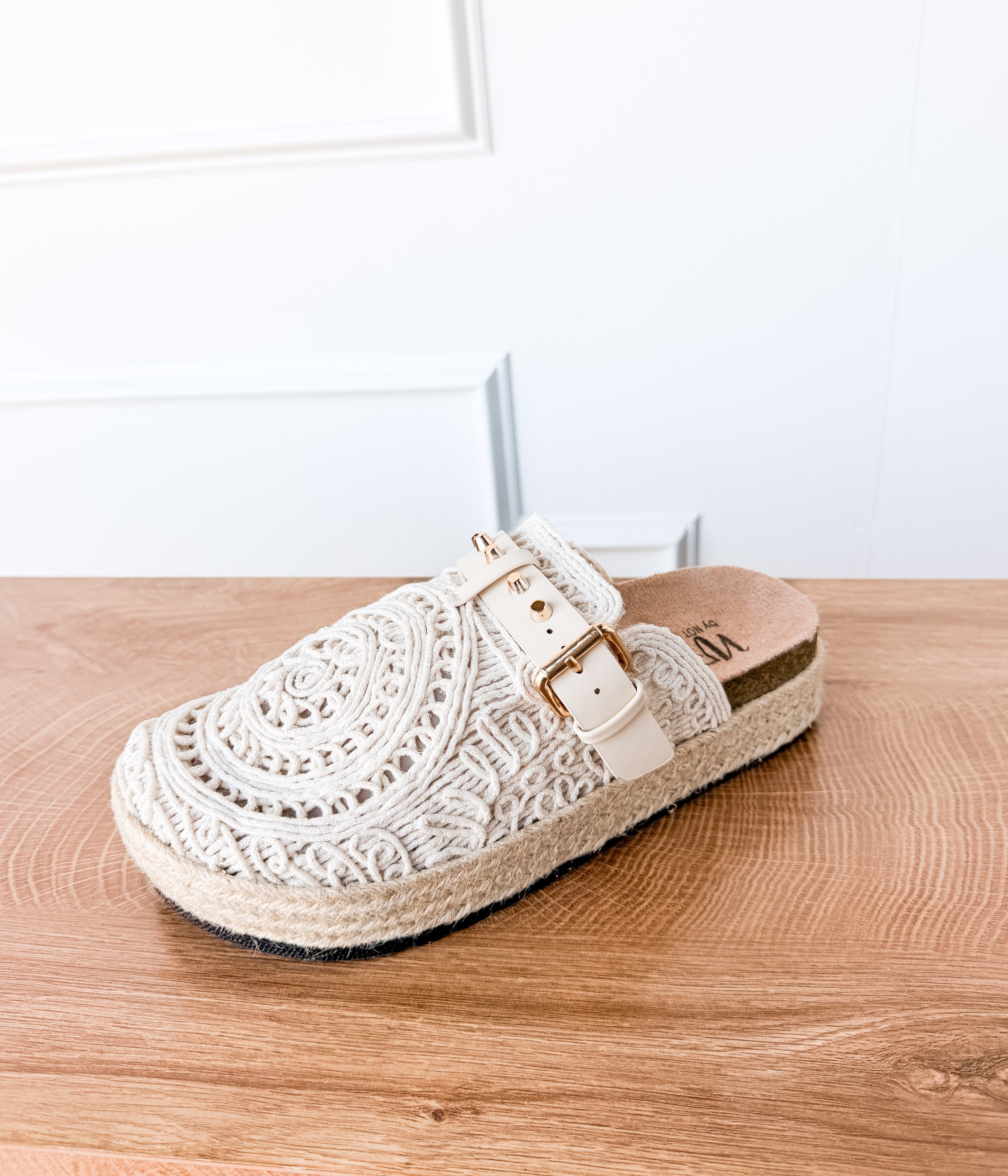White lace sandal with a buckle on a wooden surface